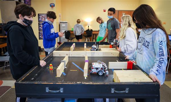 Students stand near table and watch a robot go through a maze